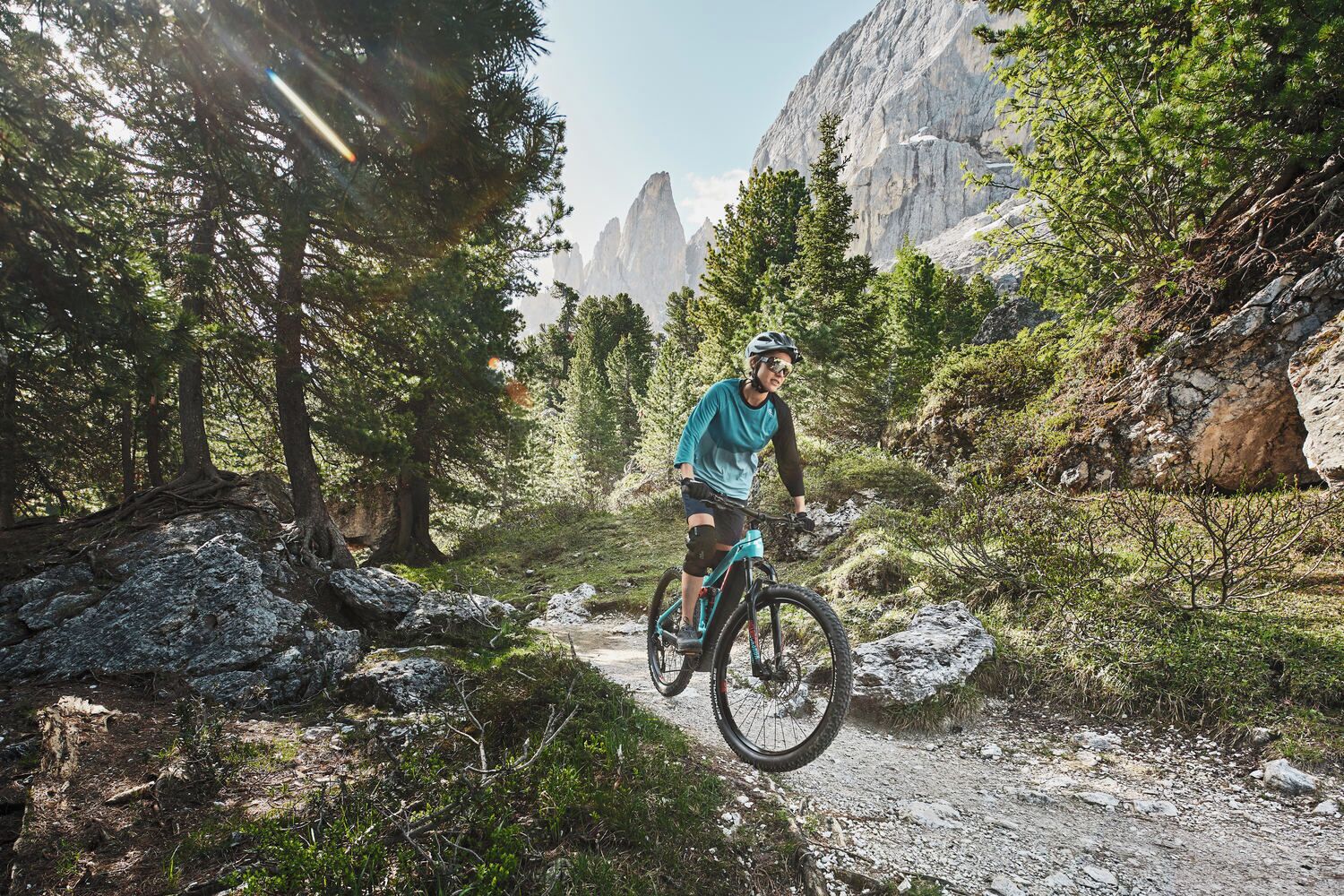 Un ciclista de montaña en un sendero rodeado de árboles y terreno rocoso.