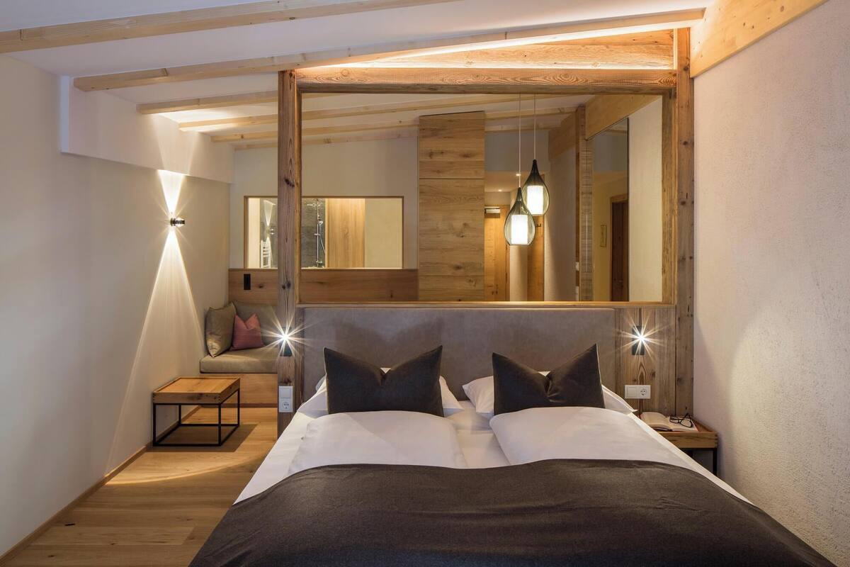 Ein Schlafzimmer mit einem großen Bett, einem Holzkopfteil, einem Nachttisch, einer Bank und einem Spiegel.