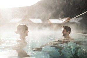 Un couple dans une piscine aux eaux cristallines, avec une chaîne de montagnes en arrière-plan.