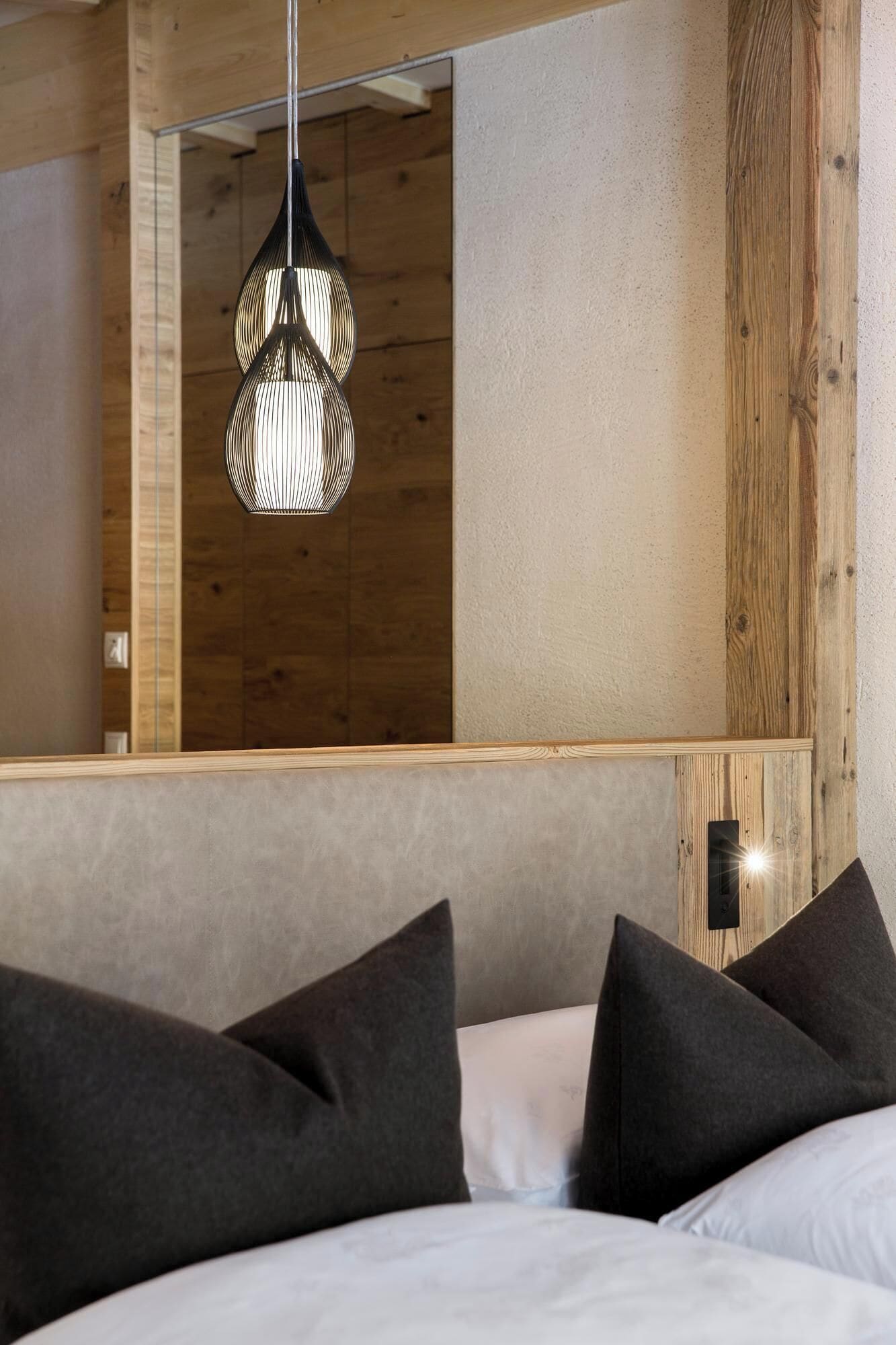 A bedroom with a large mirror, a hanging light fixture, and dark pillows.