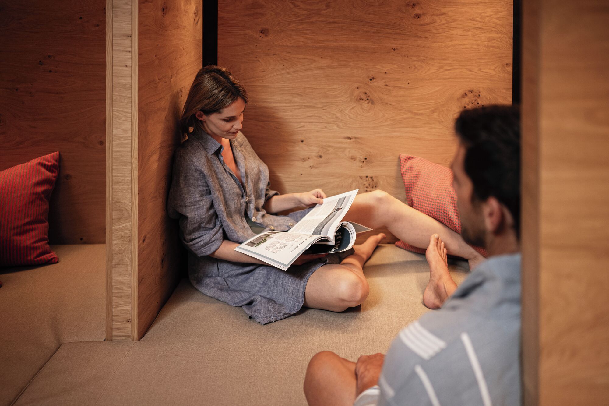 A room with a wooden floor, a sofa, and a person sitting on the floor reading a book.