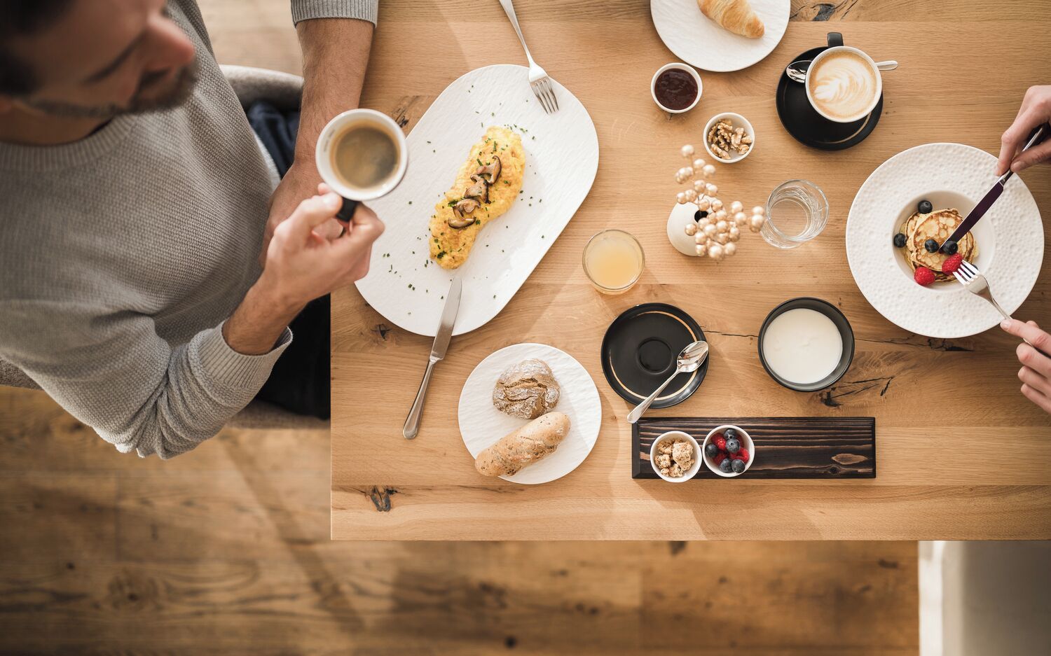 Een ontbijt met een croissant, pannenkoeken, koffie en fruit op een houten tafel.