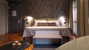 A modern hotel room with a large bed, bedside lamps, a small table, and a wall art piece. - Romantic Hotel Furno (San Francesco al Campo)