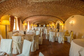 A banquet hall with tables set for a formal event, featuring arched brick ceilings and warm lighting.
