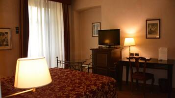 Una habitación de hotel con cama, escritorio, silla, televisor y lámpara.