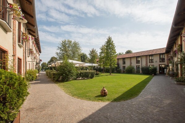 A courtyard with a cobblestone path, a grassy area, and buildings with balconies and outdoor seating.
