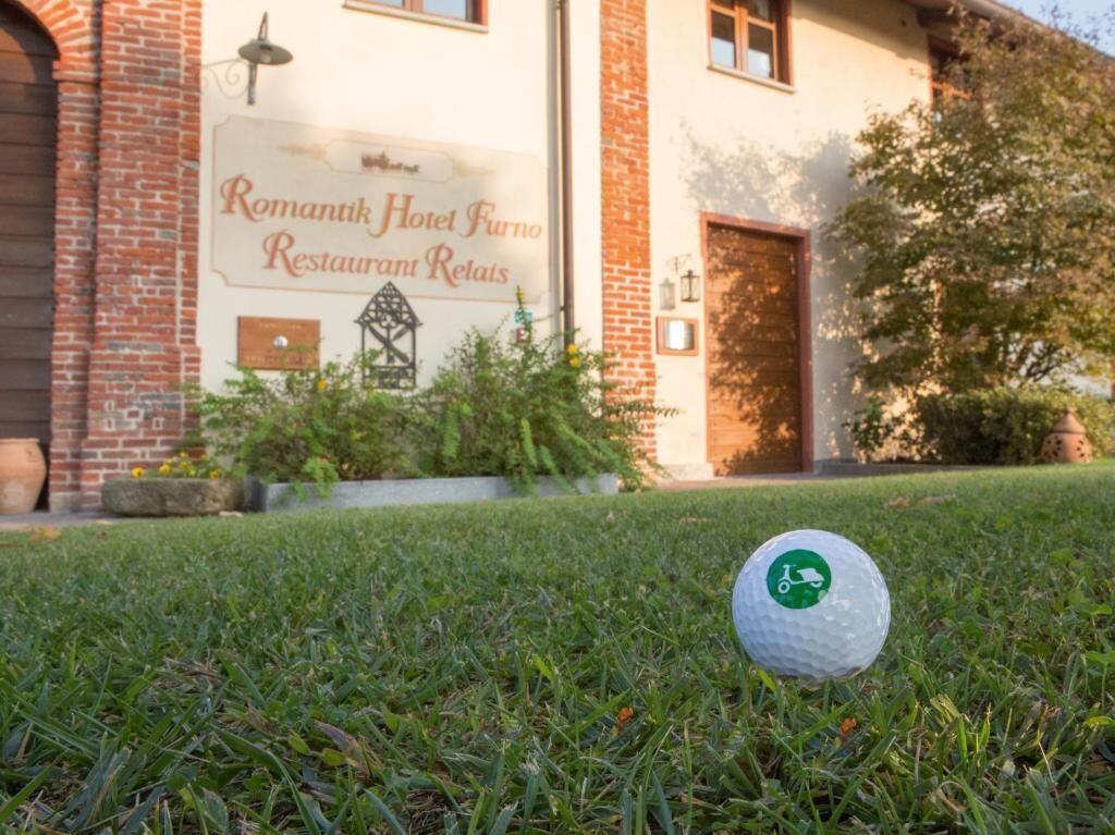 Une balle de golf sur l’herbe, devant un bâtiment sur lequel on peut lire l’inscription : « Romantik Hotel Furno Restaurant Relais ».