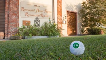 Una pallina da golf sull'erba, di fronte a un edificio con un cartello che recita 'Romantik Hotel Furno Restaurant Relais'.