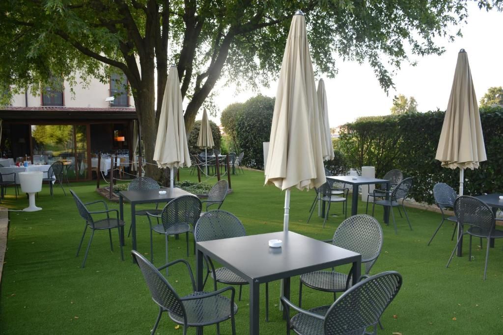 An outdoor seating area with tables and chairs, surrounded by trees and a hedge.