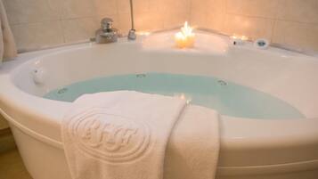 A large bathtub with a white towel draped over it, a lit candle, and a water temperature control knob.