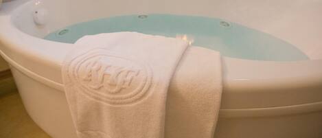 A large bathtub with a white towel draped over it, a lit candle, and a water temperature control knob.