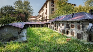 A rustic building with a stone facade and red-tiled roofs, surrounded by lush greenery. - Romantic Hotel Furno (San Francesco al Campo)