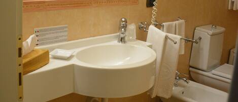 A bathroom with a sink, toilet, bidet, and a hairdryer.