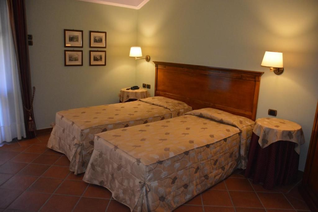 A room with two beds, a nightstand, a lamp, and a wall-mounted picture.
