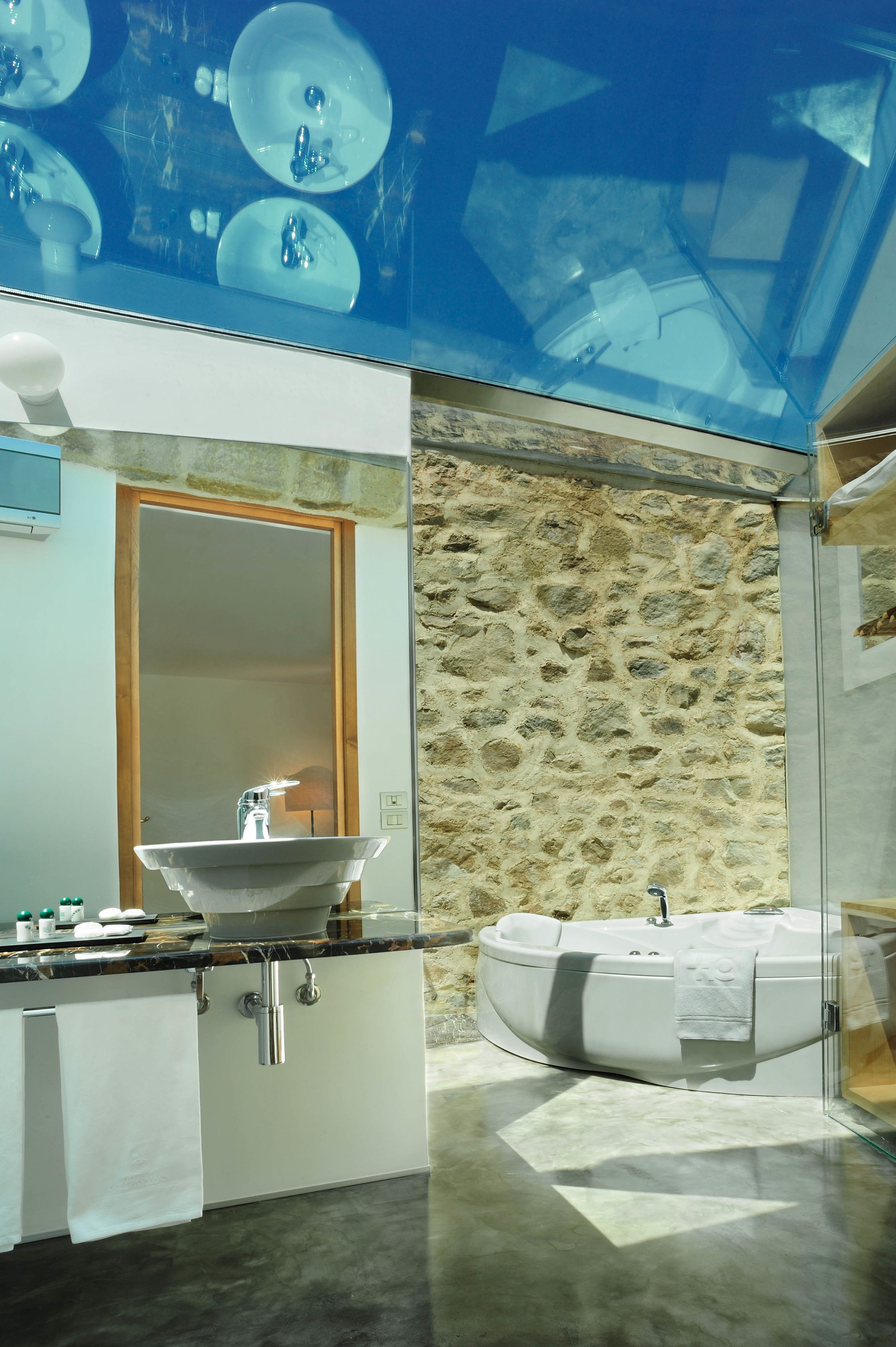 Ein modernes Badezimmer mit Steinwand, einer Glaskabine mit Badewanne und einem großen Spiegel.