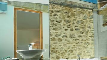 Un bagno moderno con una parete in pietra, una vasca da bagno vetrata e un grande specchio.