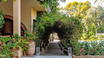 Un sendero atraviesa un exuberante jardín con plantas en macetas y un arco de ladrillo.