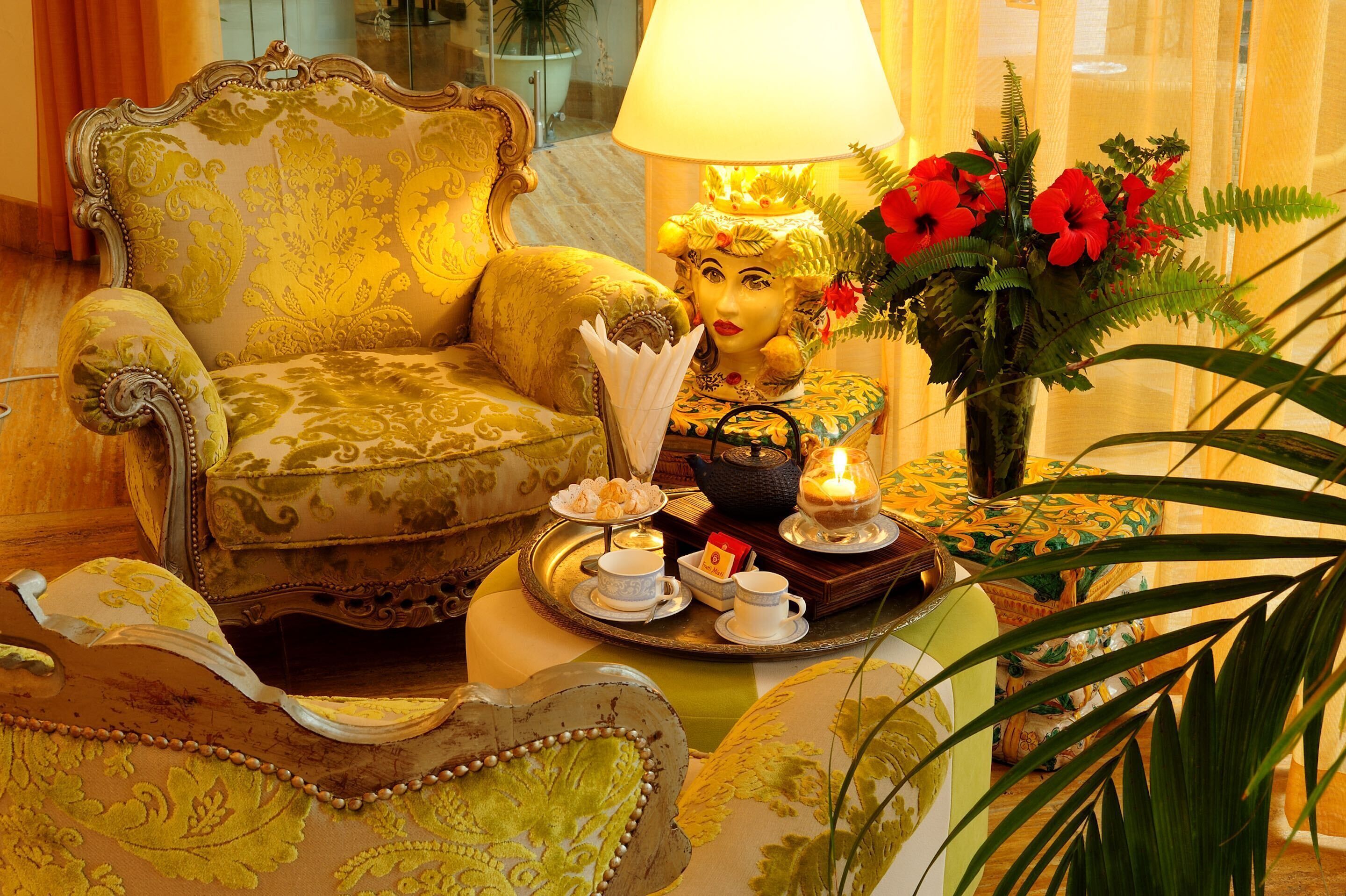 A luxurious room with an ornate armchair, a decorative lamp, a vase with red flowers, and a tray with tea set.