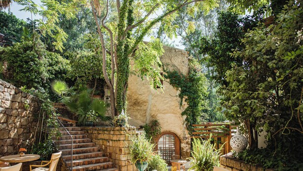 A patio with stone steps, a wooden table, wicker chairs, and potted plants. - Hotel Alberi del Paradiso (Cefalù)