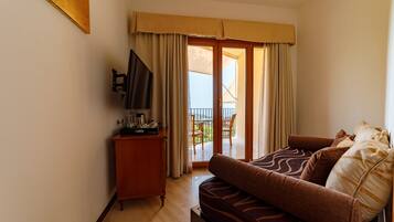 A hotel room with a sofa, a television, a small wooden cabinet, and a balcony with a table and chairs.