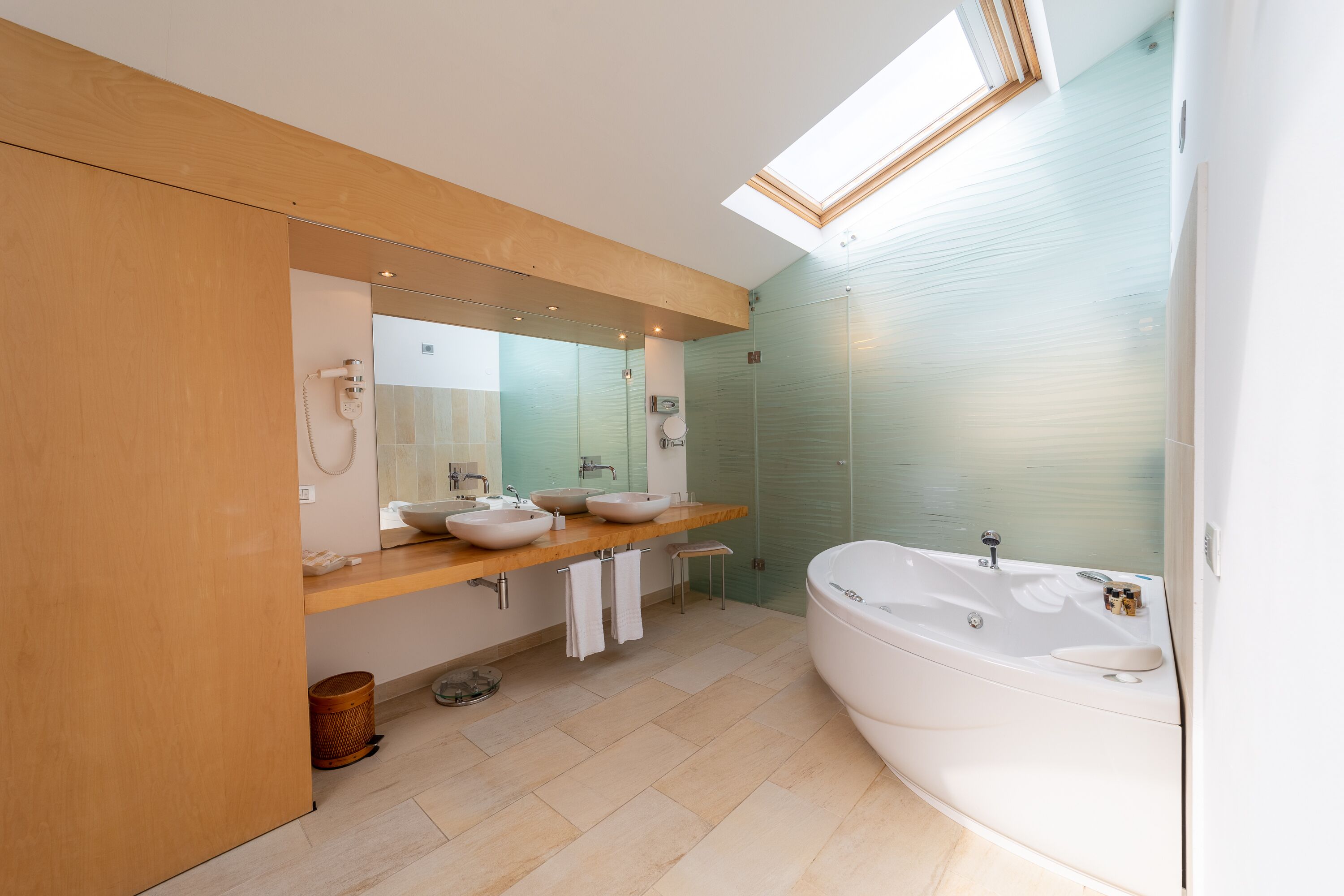 A modern bathroom with a skylight, a large bathtub, and two sinks.