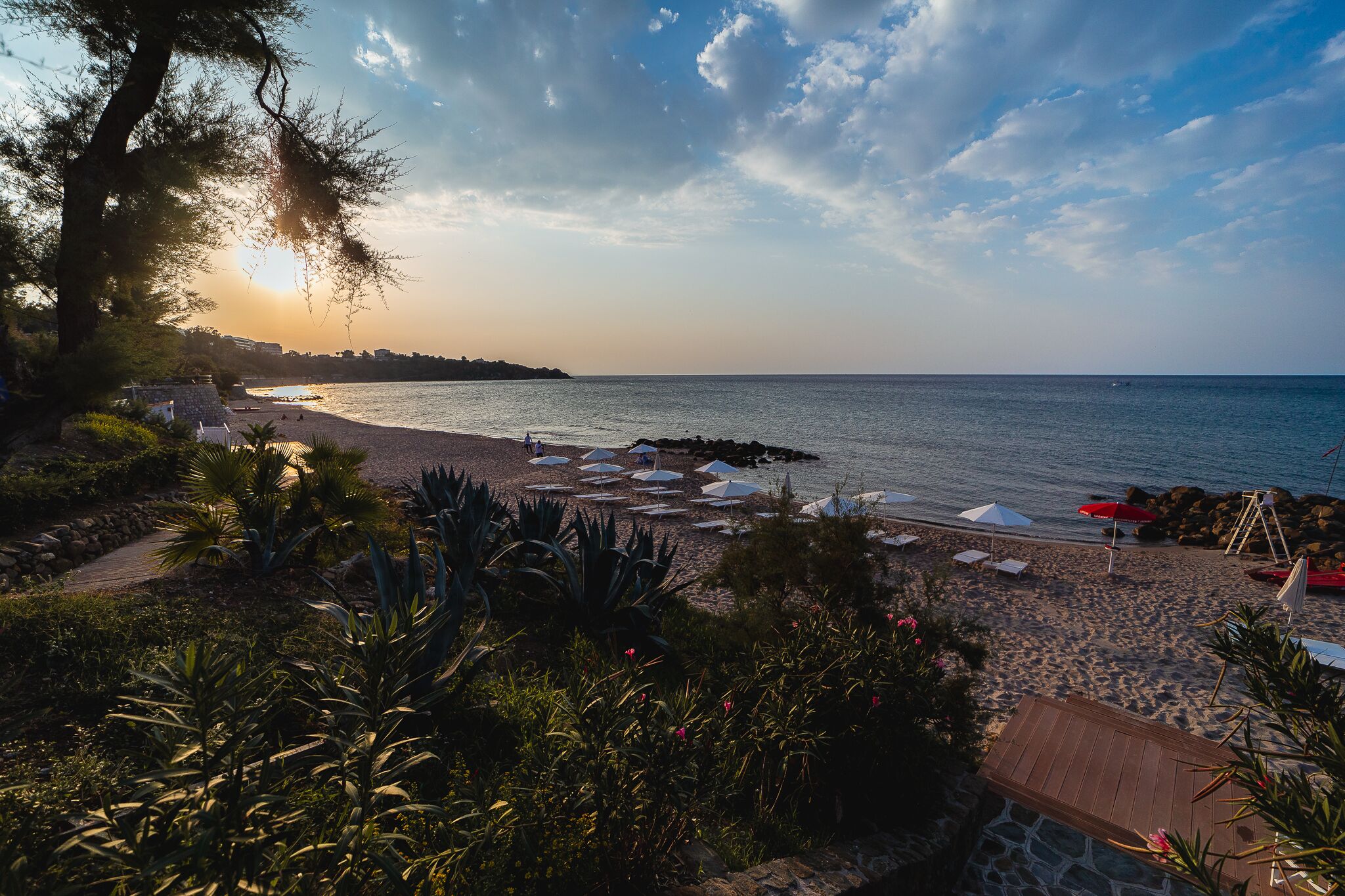 A beach with umbrellas and lounge chairs, a rocky shoreline, and a clear sky.