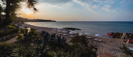 Une plage avec des parasols et des chaises longues, un rivage rocheux et un ciel dégagé.
