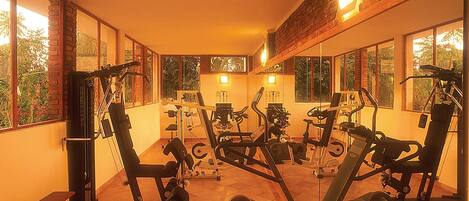 A gym with various exercise machines, large windows, and a brick wall.