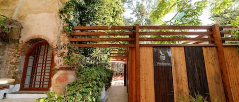 A wooden gate with a wellness sign, a stone wall, and a tiled pathway leading to a building.