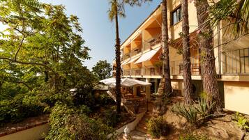 A multi-story hotel with outdoor terraces, surrounded by lush greenery and palm trees.