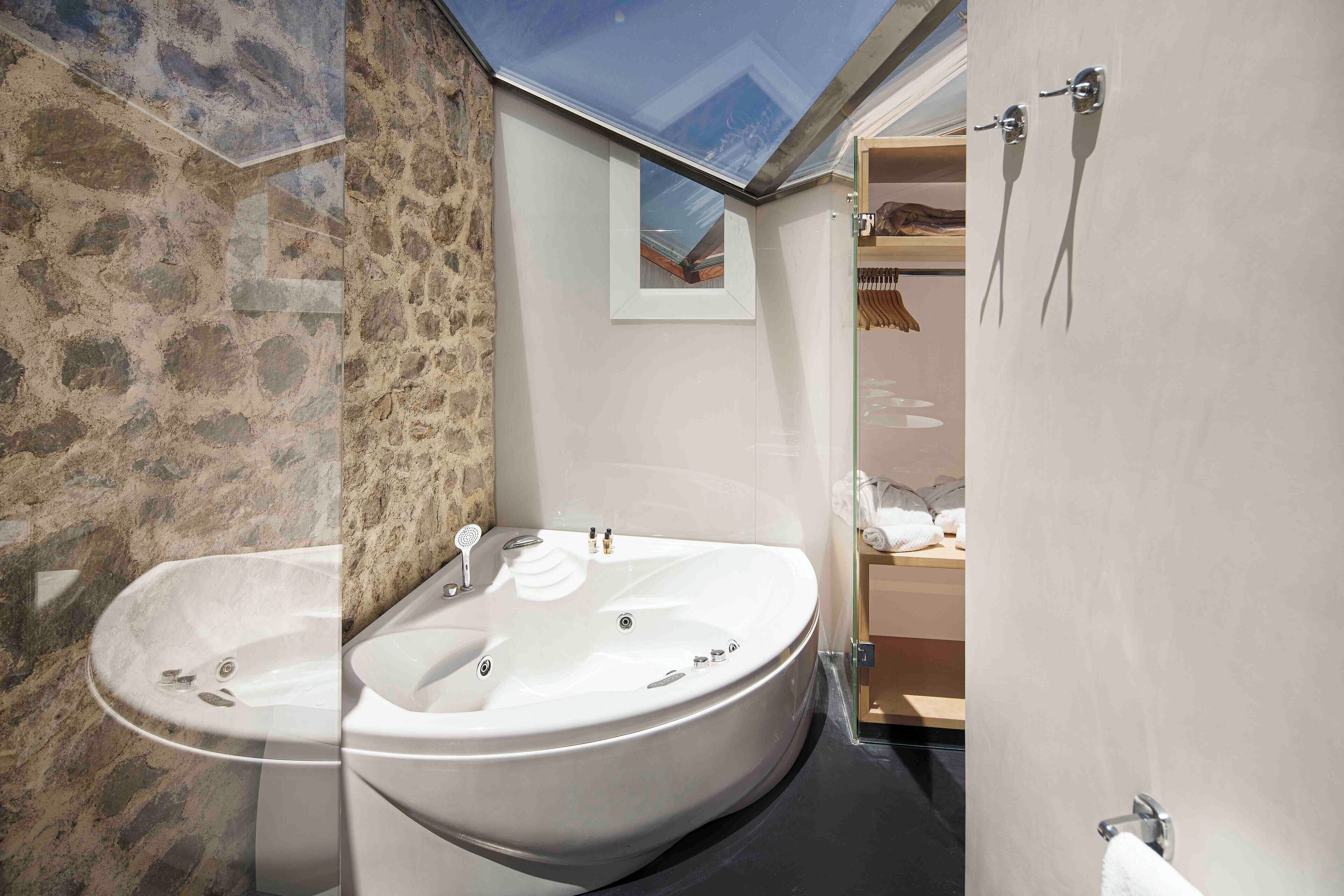 A bathroom with a stone wall, a bathtub, a sink, and a skylight.