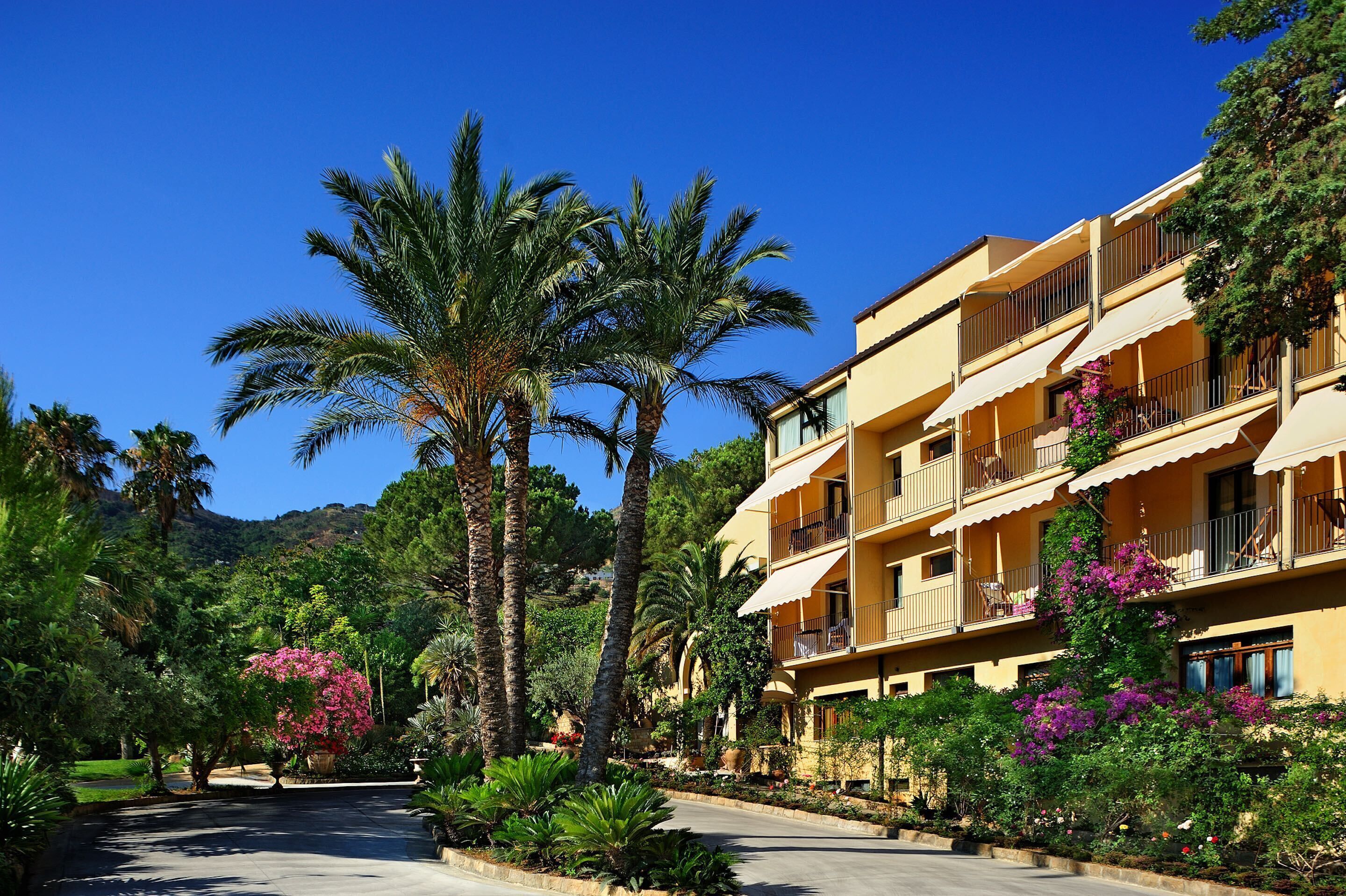 A multi-story hotel with balconies, surrounded by lush greenery and palm trees.