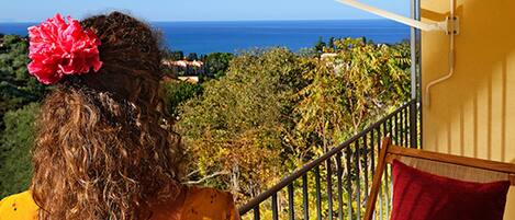 A balcony with a view of the sea, a railing, and a red cushion.
