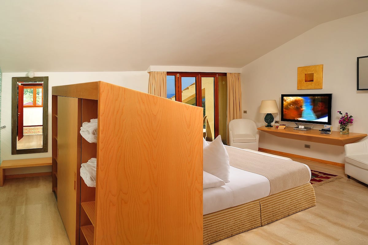 A hotel room with a bed, a TV, a desk, and a bathroom with a glass shower enclosure.