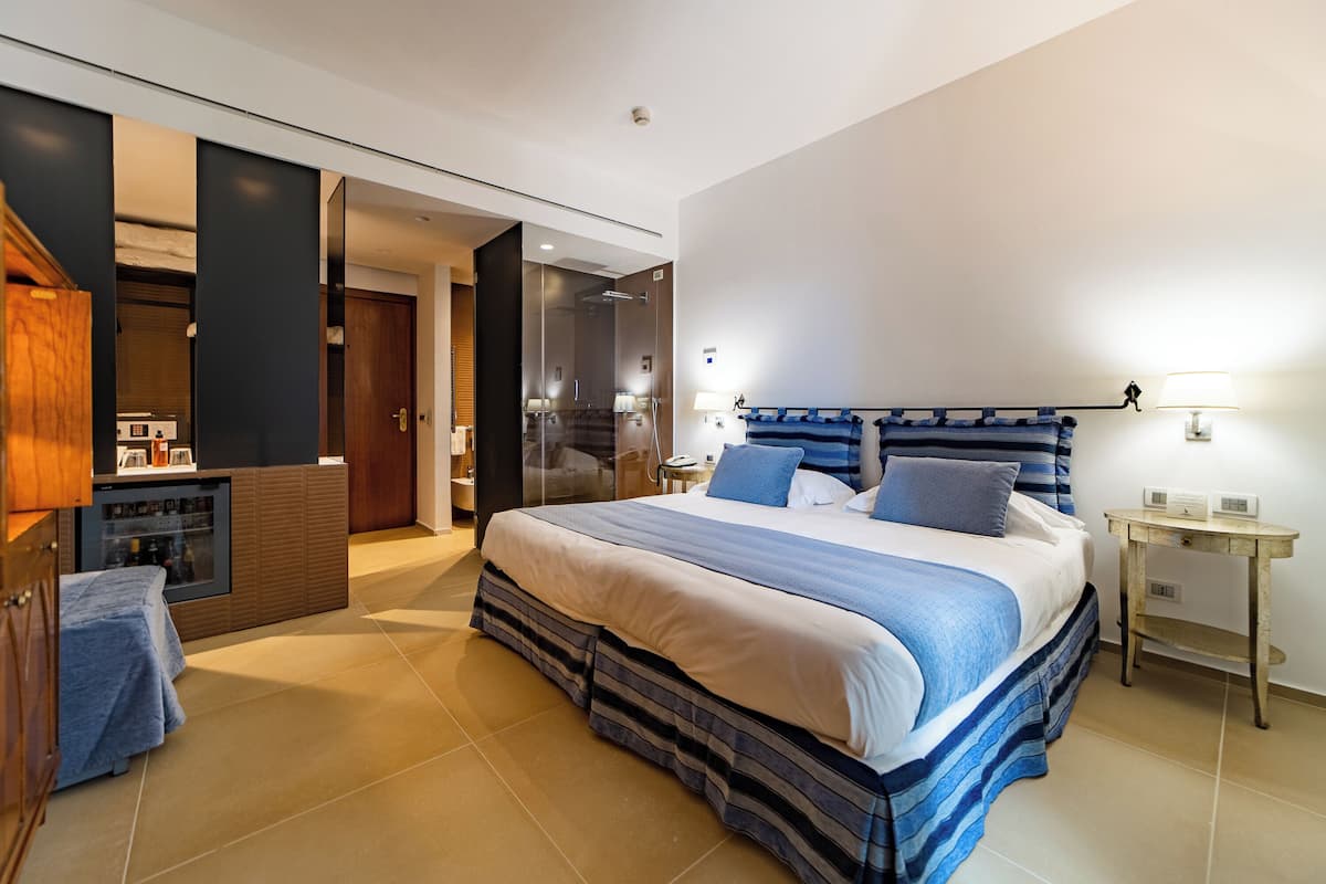 A modern hotel room with a large bed, a wooden cabinet, a small table, and a bathroom visible through an open door.