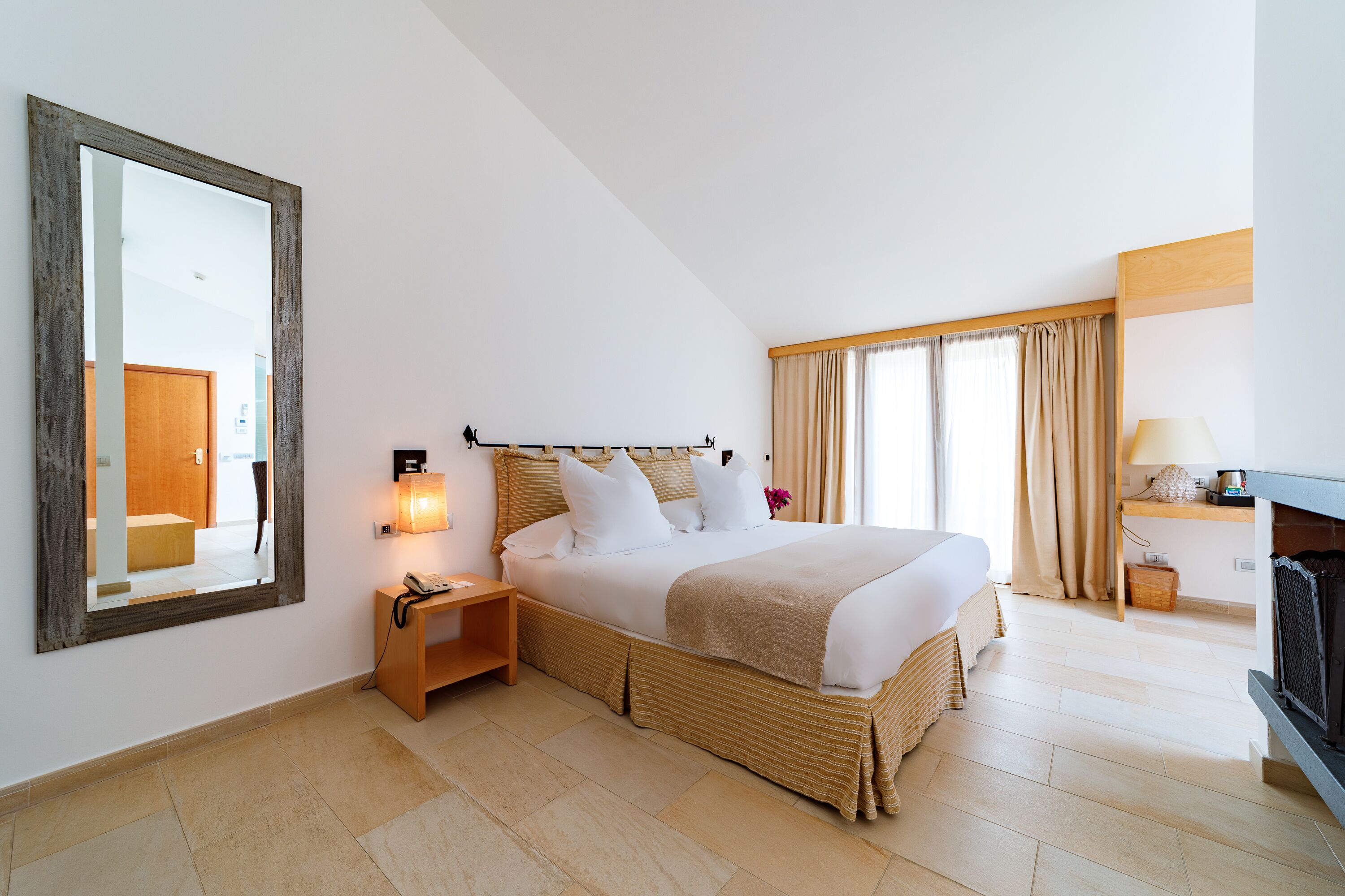 Habitación de hotel con una cama grande, una mesita de noche con lámpara, un espejo y una chimenea.