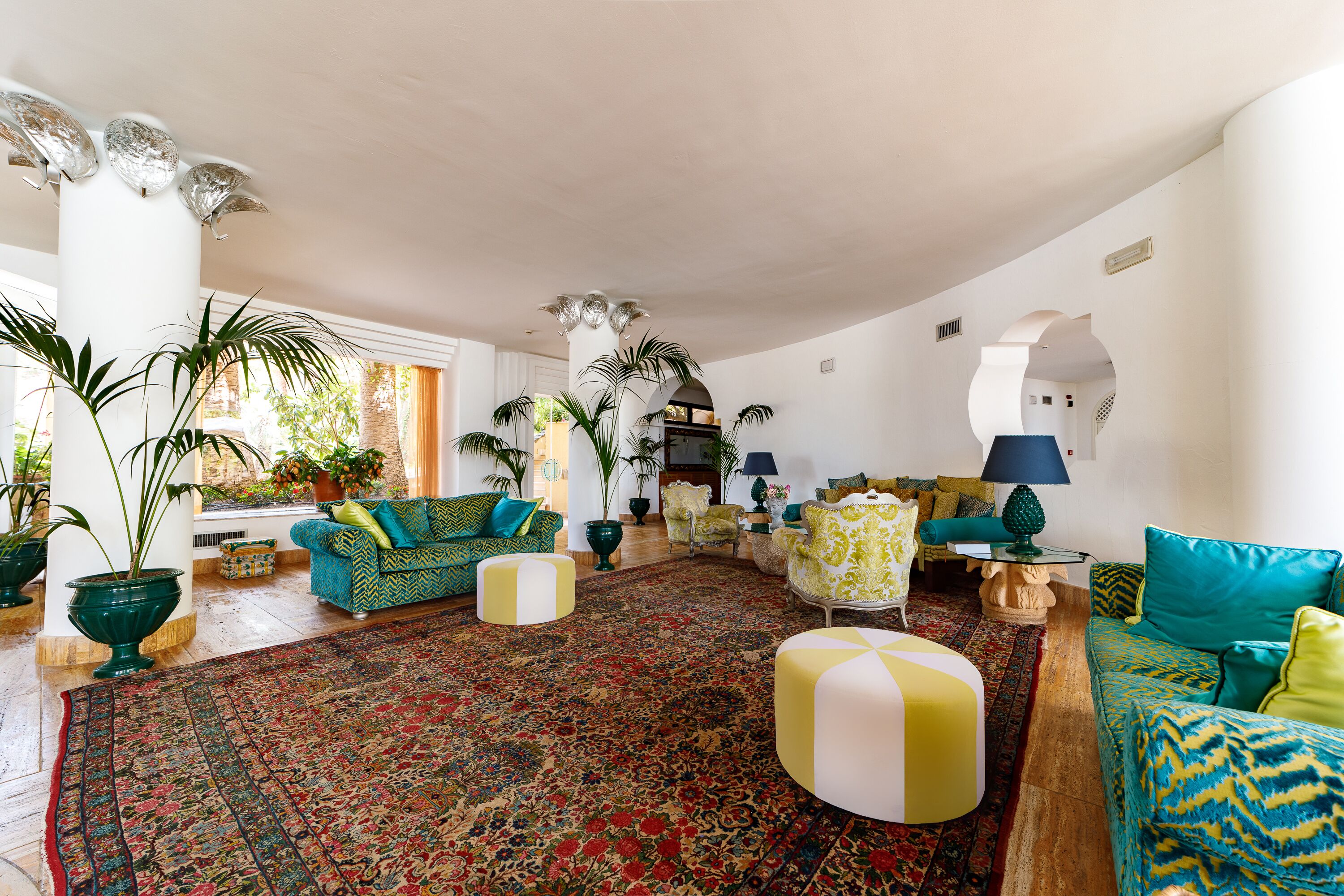 A spacious living room with a large, ornate rug, multiple seating areas, and large windows allowing natural light.