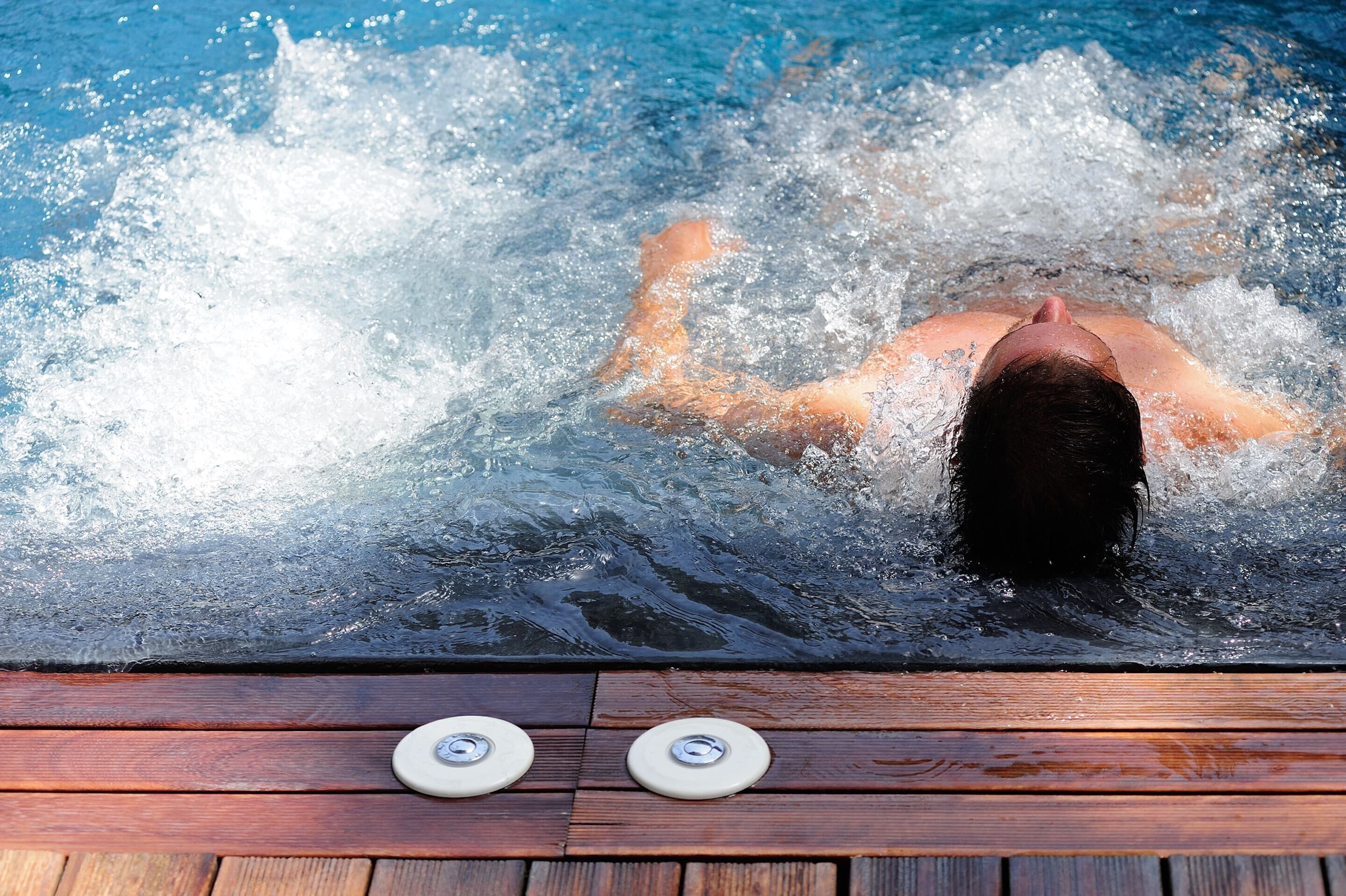 A person swimming in a pool with wooden decking and two water spigots.