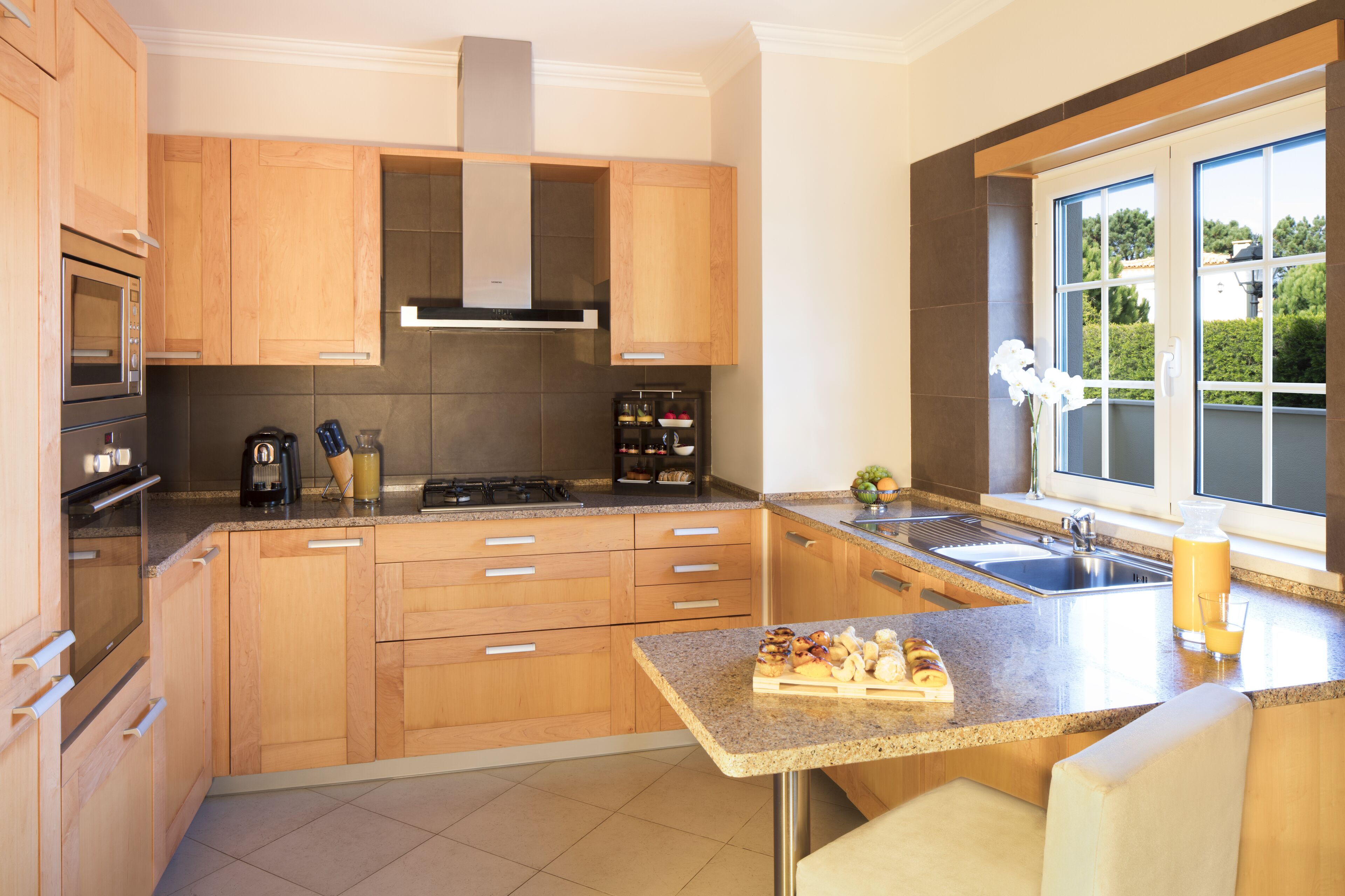 Una cocina moderna con armarios de madera, encimera de granito, horno integrado y un ventanal con vistas al exterior.