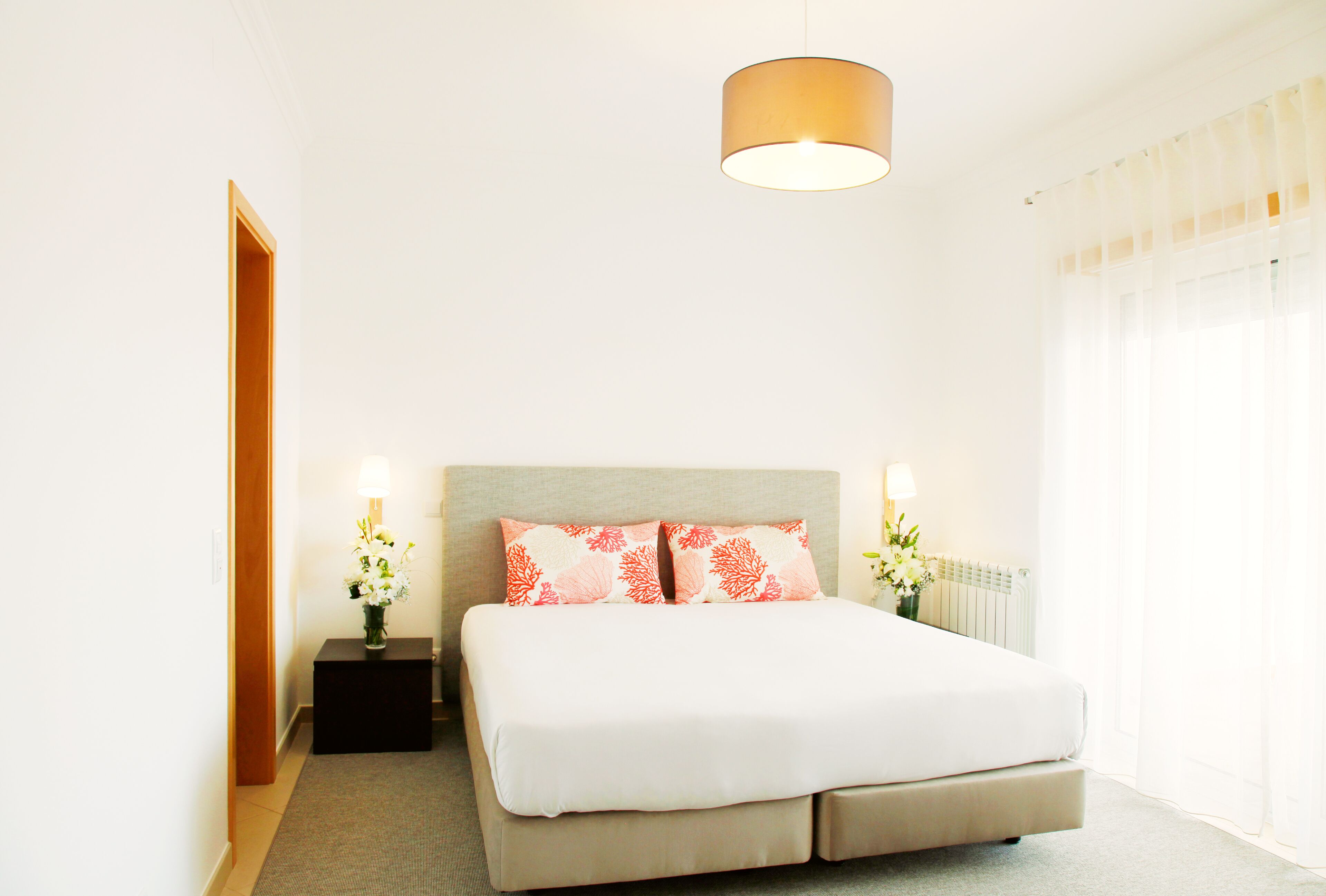Un dormitorio con cama, lámparas de noche, mesita de noche, ventana con cortinas y una lámpara colgante.
