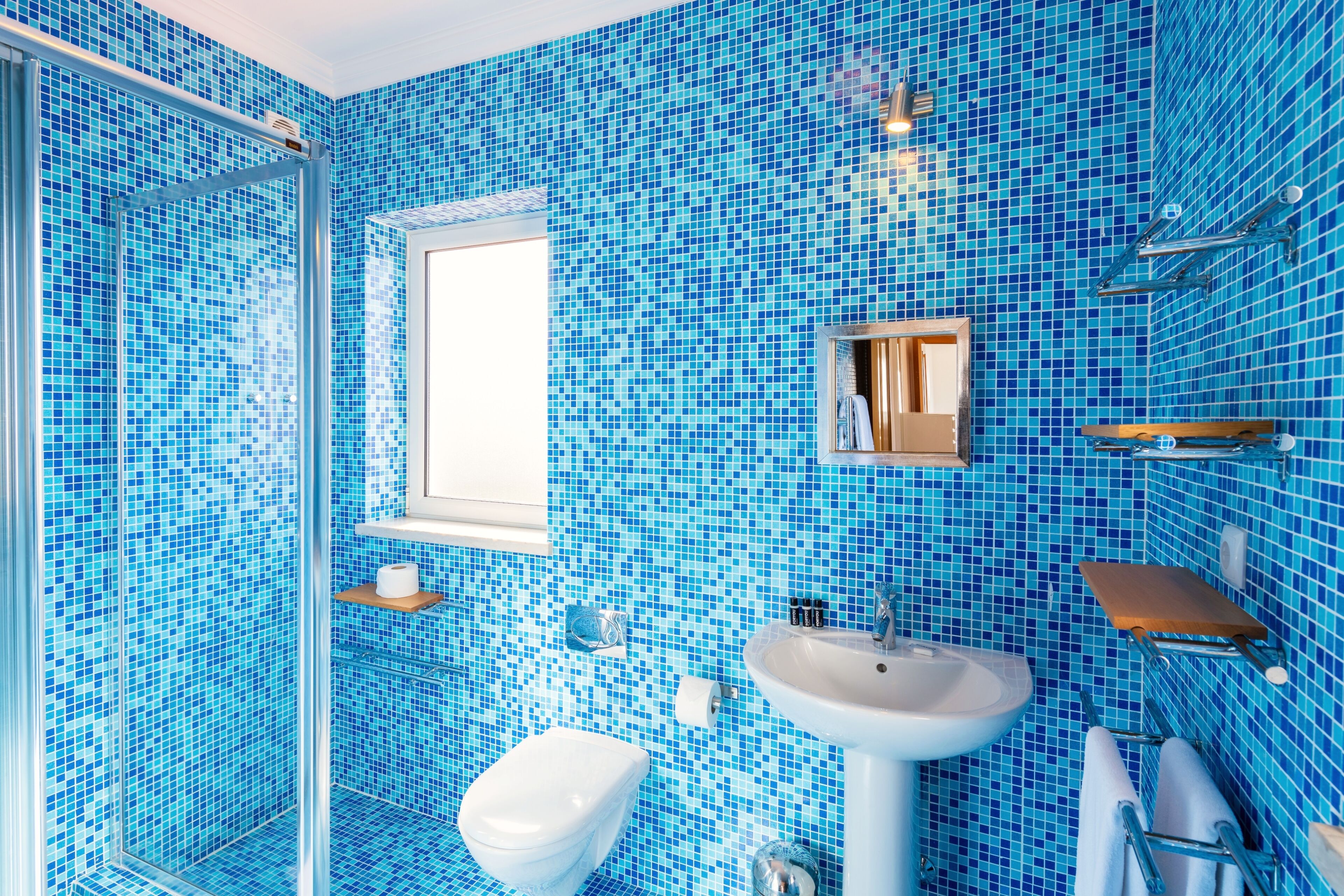 Un baño con mosaicos azules, un lavabo blanco, un inodoro y una cabina de ducha con mampara de cristal.