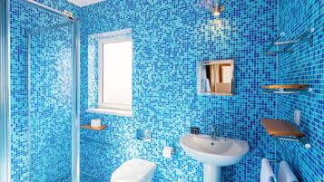 Un baño con mosaicos azules, un lavabo blanco, un inodoro y una cabina de ducha con mampara de cristal.