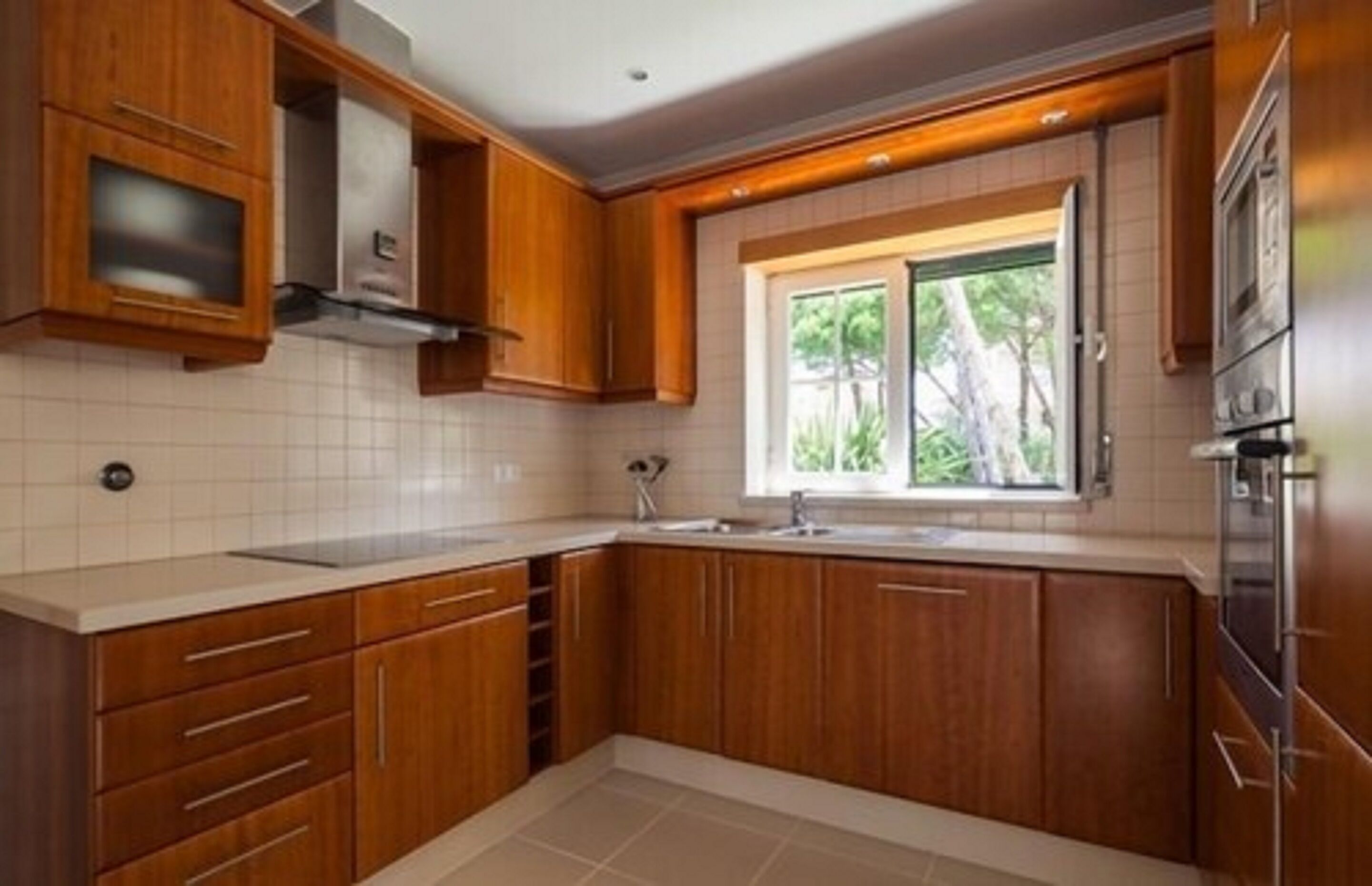A kitchen with wooden cabinets, a window, and a stainless steel refrigerator.