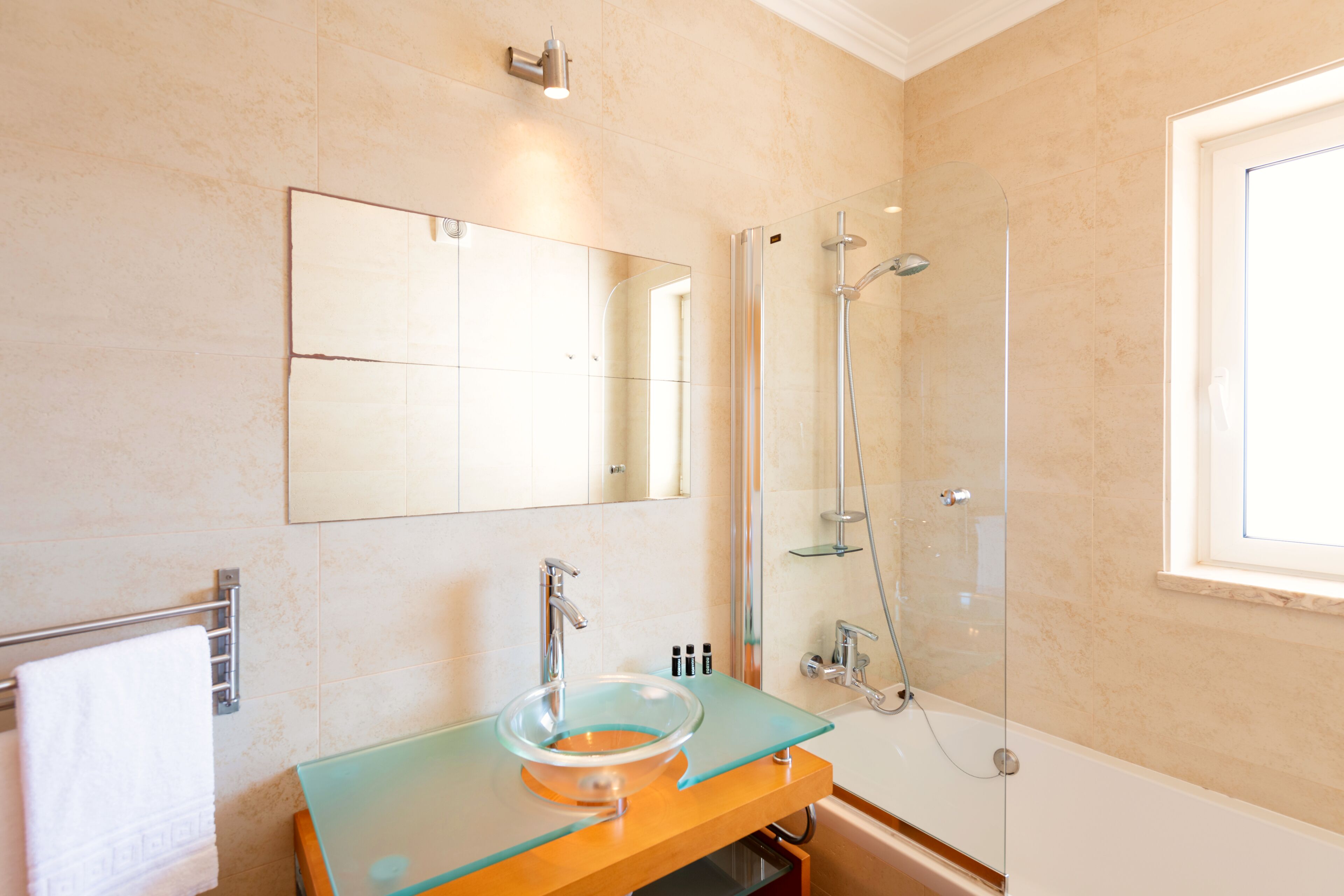 Ein modernes Badezimmer mit einem Waschbecken aus Glas, einem großen Spiegel, einer Dusche und einer Badewanne.