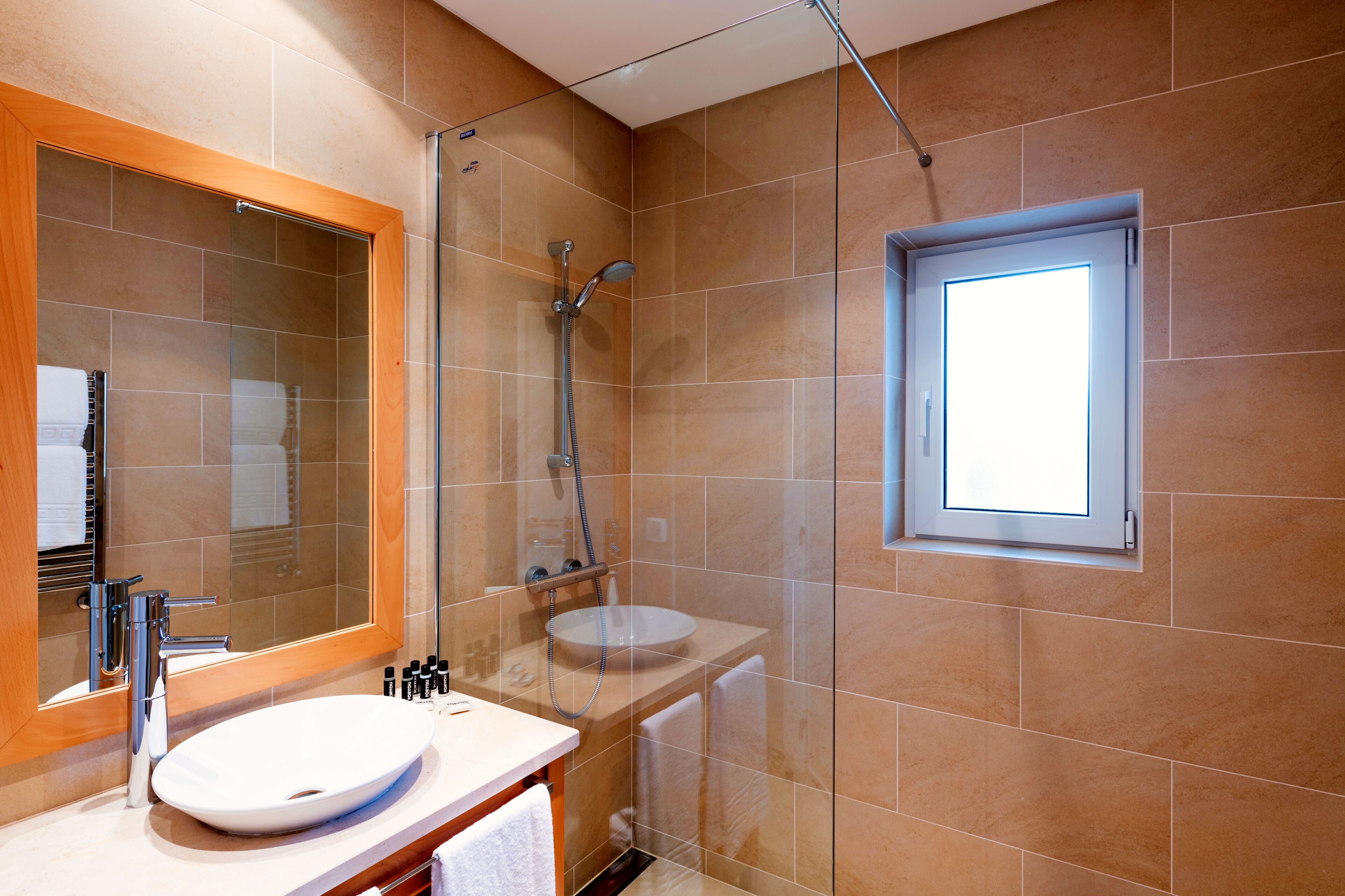Un bany modern amb dutxa de vidre, un lavabo blanc i un mirall gran.