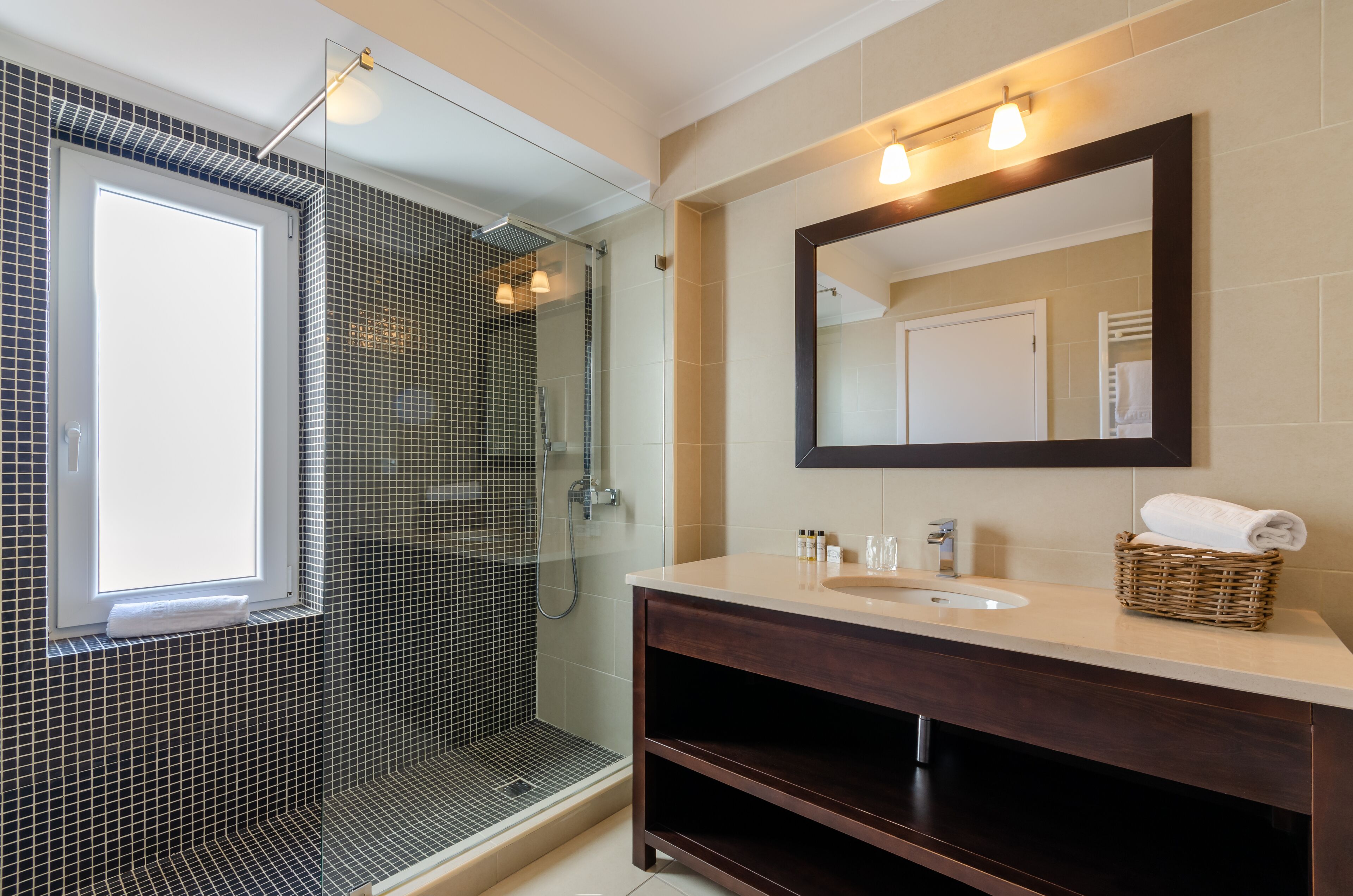 Un baño moderno con cabina de ducha de vidrio, un espejo grande y un tocador con lavabo y espacio para guardar.