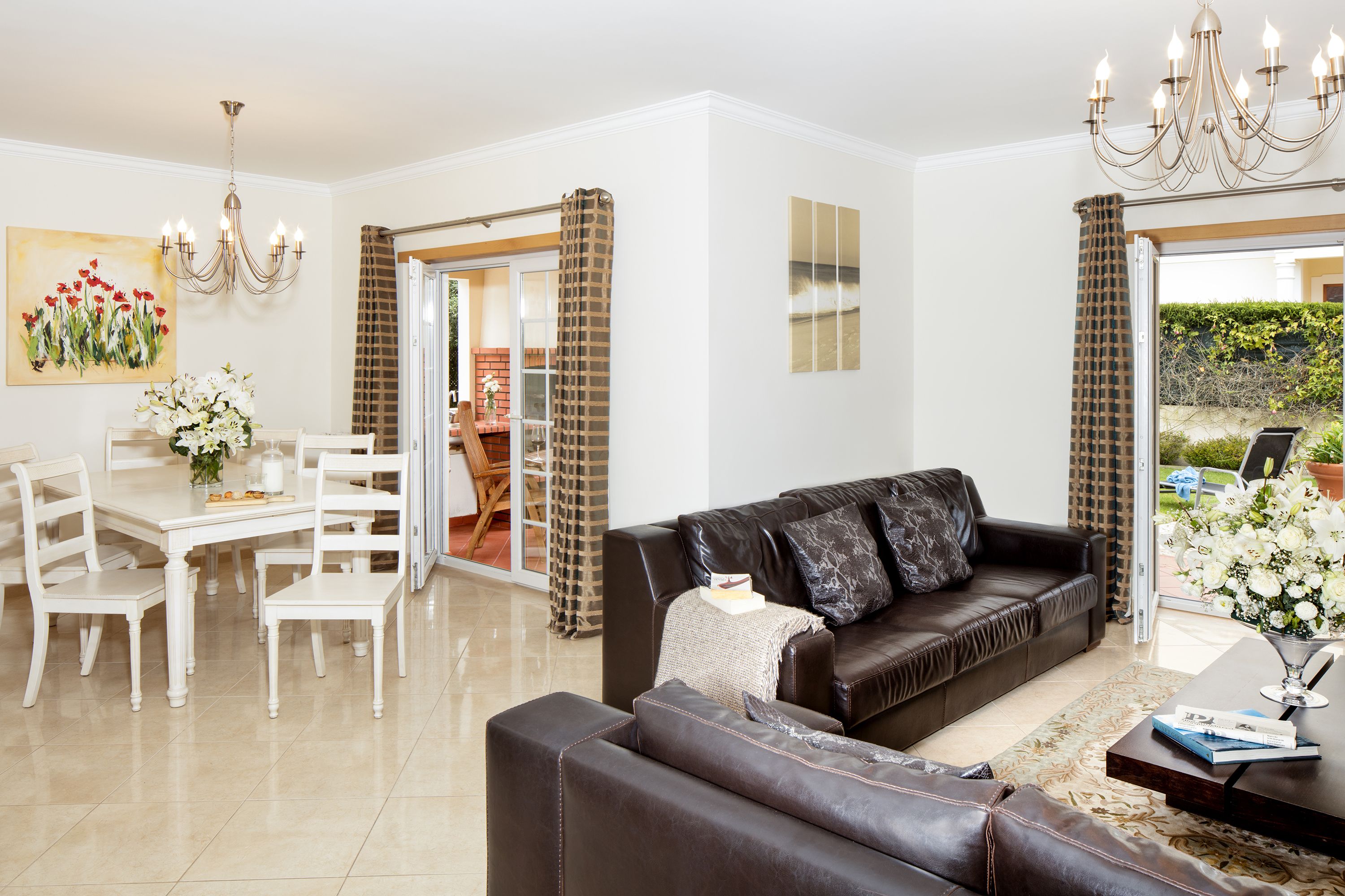 A living room with a dark brown sofa, white chairs, a dining table, and a chandelier.