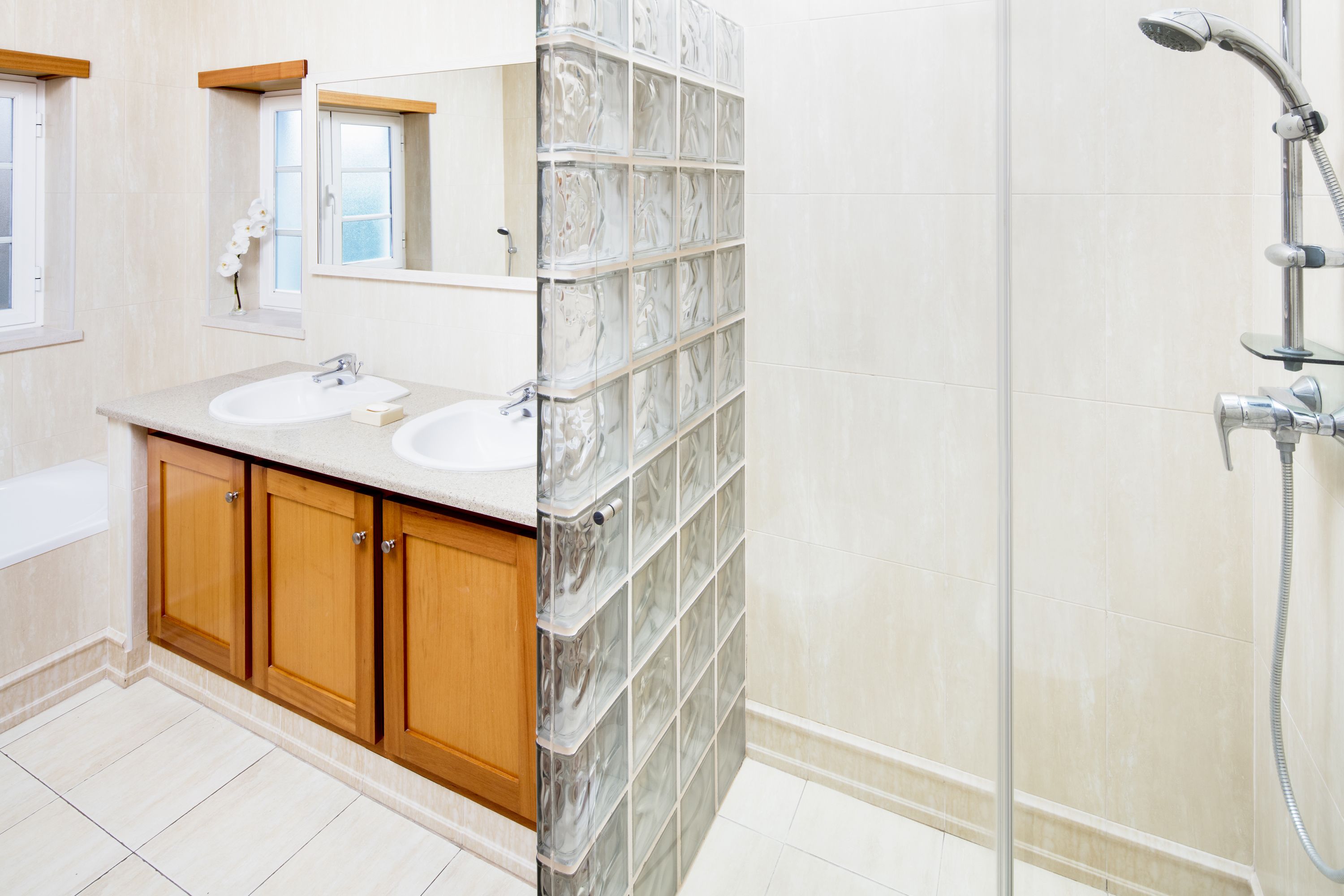 Un baño con dos lavabos, armarios de madera, cabina de ducha de vidrio y una bañera.