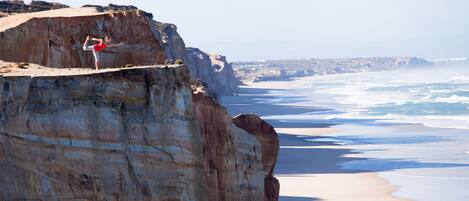 A person performing a yoga pose on a cliff overlooking a beach.