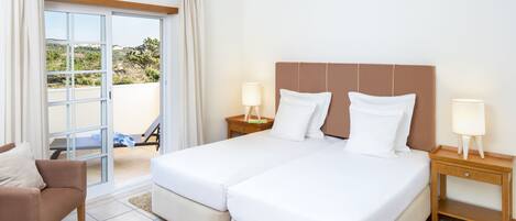 A hotel room with a double bed, two bedside tables with lamps, a chair, and a view of the outdoors through a sliding door.